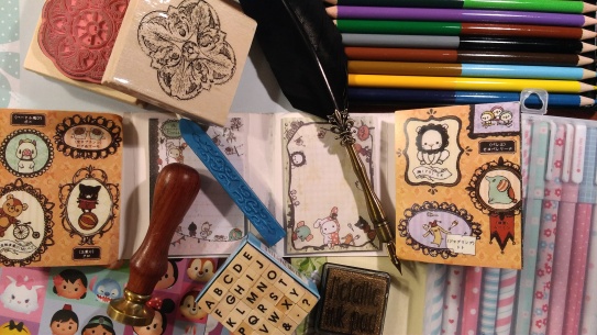 Image of scattered stationery: character sticky notes, coloured pencils, rubber stamps and ink, stickers, wax seal stamp and wax, and quill dip pen